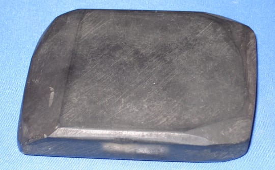 A Lydian stone: a flat, polished black slab with rounded corners and a bevelled edge, lying on blue cloth.