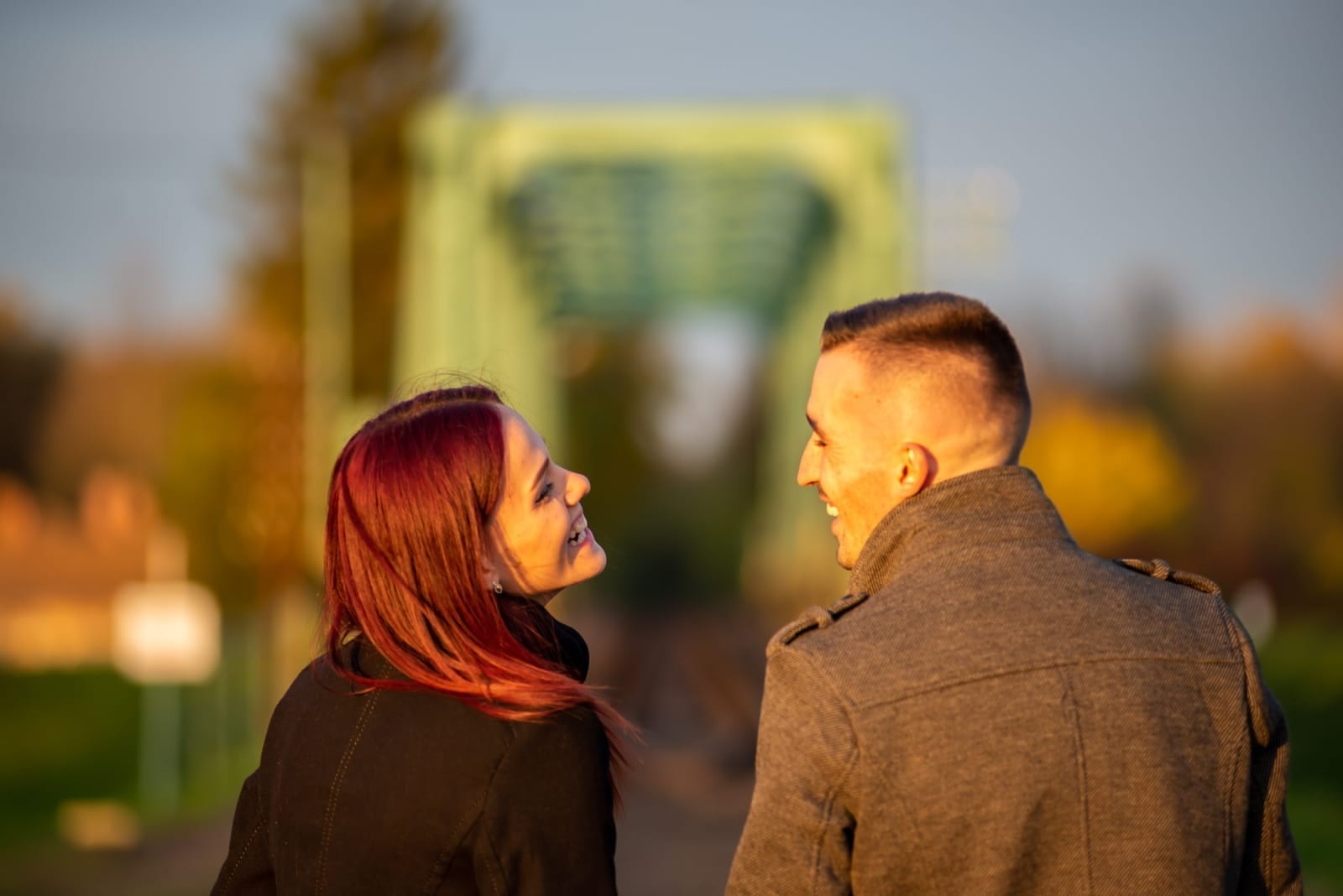 A young couple walking away from the camera at sunset, turning to look at each other and laughing