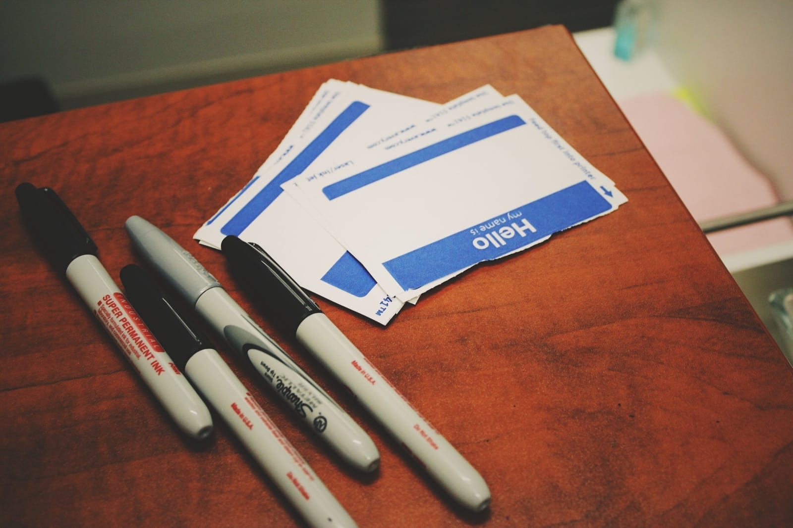 Blank 'Hello, my name is' badges fanned out on a table beside four permanent markers